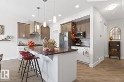 Kitchen featuring a central island with countertop seating, wood-finish flooring, two-tone cabinetry, stainless steel appliances, and pendant lighting - 