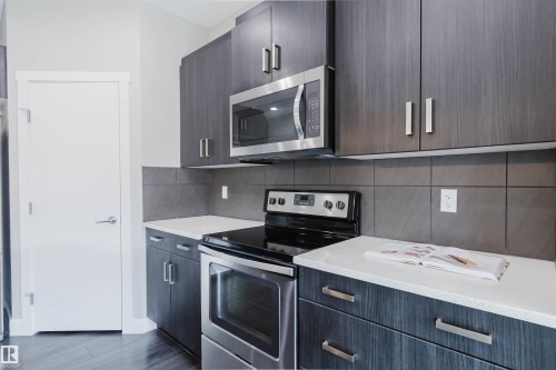 Kitchen featuring dark wood-finish cabinetry, stainless steel appliances, a built-in microwave, and light-toned countertops - 2839 Koshal Crescent, Edmonton, AB - Indoor Photo Showing Kitchen With Upgraded Kitchen