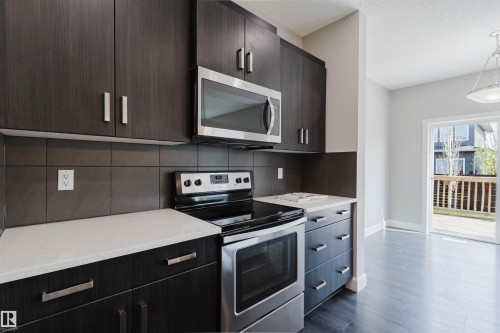 Modern kitchen with dark wood-finish cabinetry, light-colored countertops, stainless steel appliances, and a tiled backsplash - 2839 Koshal Crescent, Edmonton, AB - Indoor Photo Showing Kitchen With Upgraded Kitchen
