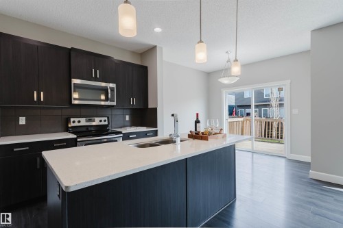 Spacious kitchen featuring dark wood-finish cabinetry, stainless steel appliances, a center island with an undermount sink, and light-toned countertops - 2839 Koshal Crescent, Edmonton, AB - Indoor Photo Showing Kitchen With Double Sink With Upgraded Kitchen