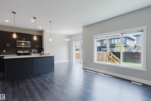 Open-concept living area featuring wood-finish flooring, a contemporary kitchen island with white countertops, dark cabinetry, and stainless steel appliances - 2839 Koshal Crescent, Edmonton, AB - Indoor Photo Showing Kitchen