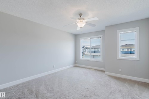 Spacious room featuring light gray walls, white trim, two windows providing natural illumination, textured ceiling, and a ceiling fan with integrated lighting - 2839 Koshal Crescent, Edmonton, AB - Indoor Photo Showing Other Room