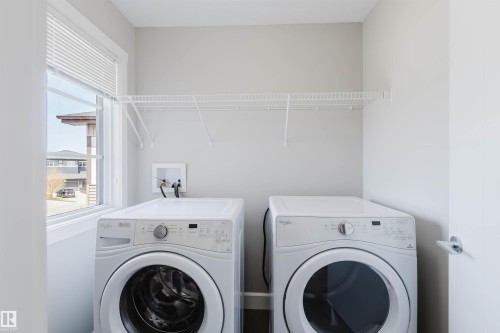 Laundry room featuring a front-loading washer and dryer, a window with blinds, and a wall-mounted wire shelf - 2839 Koshal Crescent, Edmonton, AB - Indoor Photo Showing Laundry Room