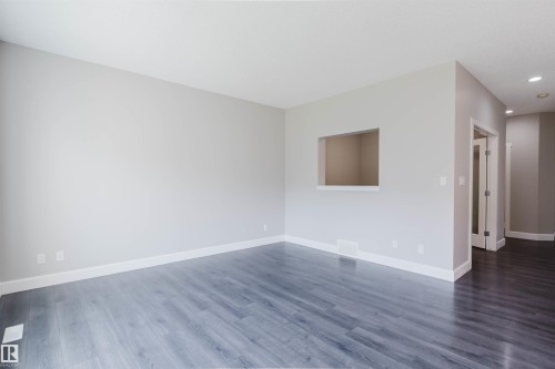 Spacious interior featuring a neutral color palette, wood-finish flooring, a pass-through window, recessed lighting, and white baseboards - 2839 Koshal Crescent, Edmonton, AB - Indoor Photo Showing Other Room