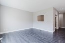 Spacious interior featuring a neutral color palette, wood-finish flooring, a pass-through window, recessed lighting, and white baseboards - 2839 Koshal Crescent, Edmonton, AB  - Indoor Photo Showing Other Room 