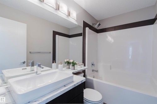 Bathroom featuring a dual vessel sink vanity with a marble-finish countertop, a full-width mirror, and a white tub/shower combination with dark accent tiling - 2839 Koshal Crescent, Edmonton, AB - Indoor Photo Showing Bathroom