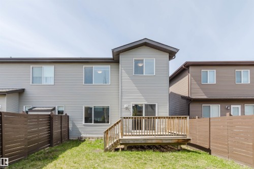 Rear exterior of a light-colored vinyl-sided residence featuring a wooden deck with railing, a grass lawn, and wood privacy fencing - 2839 Koshal Crescent, Edmonton, AB - Outdoor With Deck Patio Veranda With Exterior