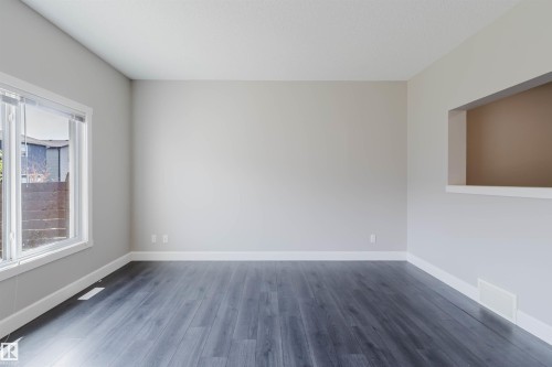 Spacious room featuring dark wood-finish flooring, light neutral-toned walls, white baseboards, and a large window with white trim - 2839 Koshal Crescent, Edmonton, AB - Indoor Photo Showing Other Room