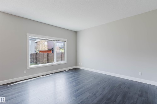 Spacious room featuring dark wood-finish flooring, light gray wall paint, white baseboards, and a large window with white trim - 2839 Koshal Crescent, Edmonton, AB - Indoor Photo Showing Other Room