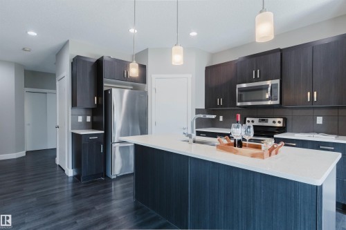 Modern kitchen featuring dark wood-finish cabinetry, stainless steel appliances, a center island with a white countertop, and pendant lighting fixtures - 2839 Koshal Crescent, Edmonton, AB - Indoor Photo Showing Kitchen With Stainless Steel Kitchen With Upgraded Kitchen