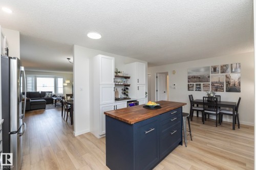 Bright kitchen and dining area featuring a dark blue island with a wood-finish countertop, stainless steel appliances, white cabinetry, and wood-finish flooring - 25 1904 Mill Woods Road Road, Edmonton, AB - Indoor Photo Showing Kitchen