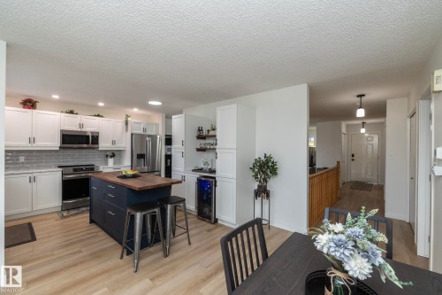 Modern kitchen featuring white cabinetry, stainless steel appliances, a dark blue island with a wood-finish countertop, light wood-finish flooring, and subway tile backsplash - 25 1904 Mill Woods Road Road, Edmonton, AB - Indoor Photo Showing Kitchen With Upgraded Kitchen