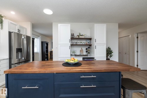 Kitchen featuring a large blue island with a wood countertop, integrated stainless steel refrigerator, white cabinetry, and open shelving - 25 1904 Mill Woods Road Road, Edmonton, AB - Indoor Photo Showing Kitchen