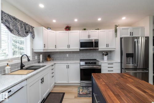 Modern kitchen featuring white shaker cabinetry, stainless steel appliances, light-toned countertops, subway tile backsplash, and a central island with a wood-finish top - 25 1904 Mill Woods Road Road, Edmonton, AB - Indoor Photo Showing Kitchen With Double Sink With Upgraded Kitchen