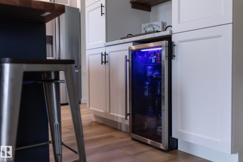 Integrated beverage cooler with illuminated interior, set within white shaker-style cabinetry with matte black hardware - 25 1904 Mill Woods Road Road, Edmonton, AB - Indoor