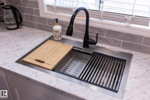 Undermount stainless steel sink with integrated cutting board and drying rack, featuring a matte black gooseneck faucet - 25 1904 Mill Woods Road Road, Edmonton, AB - Indoor