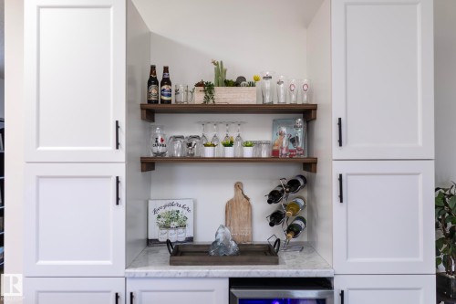 Built-in beverage station featuring white shaker-style cabinetry with matte black hardware, open wood shelving, a marble-look countertop, and an integrated beverage refrigerator - 25 1904 Mill Woods Road Road, Edmonton, AB - Indoor Photo Showing Other Room