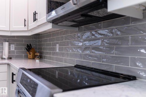 Modern kitchen featuring white cabinetry with matte black hardware, light-toned countertops, a glass top electric range, a stainless steel microwave, and a gray subway tile backsplash - 25 1904 Mill Woods Road Road, Edmonton, AB - Indoor Photo Showing Kitchen