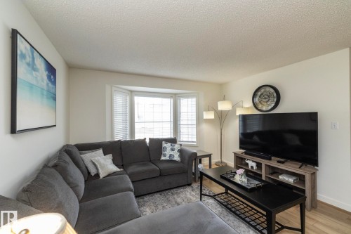 Living area featuring a bay window with horizontal blinds, cream-colored walls, wood-finish flooring, and a textured ceiling - 25 1904 Mill Woods Road Road, Edmonton, AB - Indoor Photo Showing Living Room