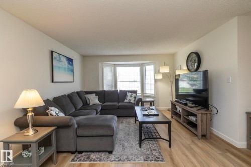 Bright living area featuring wood-finish flooring, a bay window with blinds, and light-toned walls - 25 1904 Mill Woods Road Road, Edmonton, AB - Indoor Photo Showing Living Room