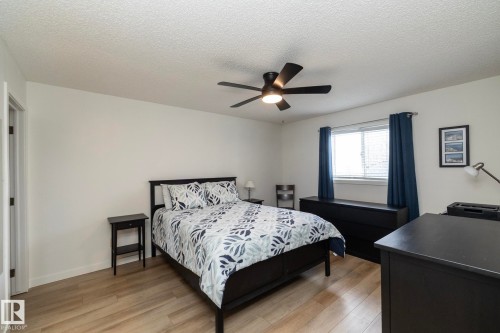 Bright interior space featuring wood-finish flooring, a contemporary ceiling fan with integrated lighting, and a large window with privacy blinds - 25 1904 Mill Woods Road Road, Edmonton, AB - Indoor Photo Showing Bedroom