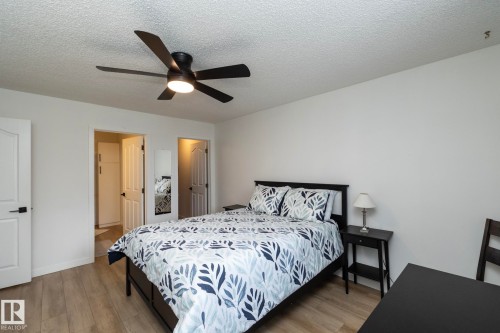 Bedroom featuring a ceiling fan with integrated lighting, wood-finish flooring, and white paneled doors with black hardware - 25 1904 Mill Woods Road Road, Edmonton, AB - Indoor Photo Showing Bedroom
