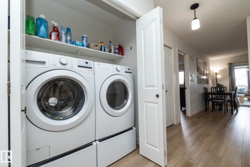 Dedicated laundry area featuring a front-loading washer and dryer, elevated on pedestals for convenience, with an overhead storage shelf - 25 1904 Mill Woods Road Road, Edmonton, AB - Indoor Photo Showing Laundry Room