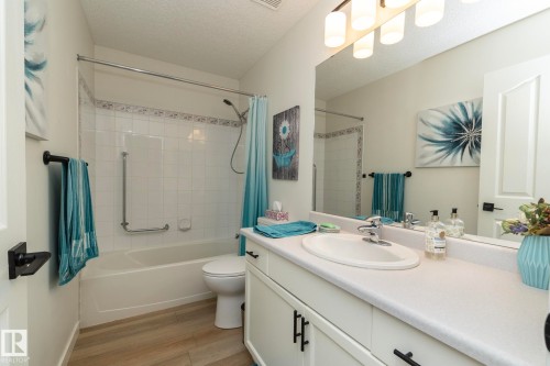 Bathroom featuring a white vanity with an integrated sink, a large mirror, and a white tiled shower-over-tub with decorative border tiles - 25 1904 Mill Woods Road Road, Edmonton, AB - Indoor Photo Showing Bathroom