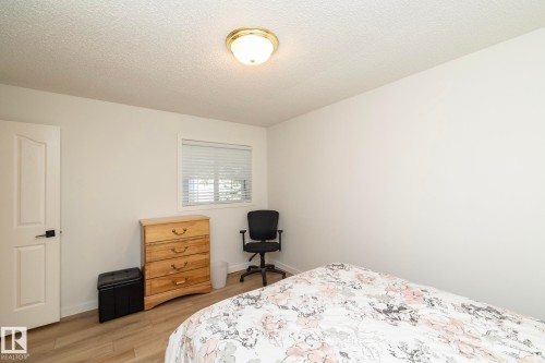 Interior room featuring light-toned wood-finish flooring, a white paneled door with black hardware, and a window with horizontal blinds - 25 1904 Mill Woods Road Road, Edmonton, AB - Indoor Photo Showing Bedroom