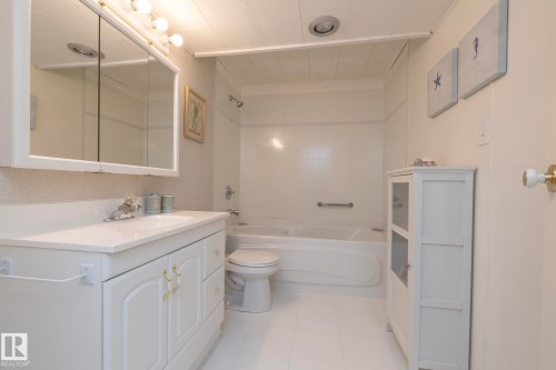 Bathroom featuring a white vanity with integrated sink, gold-toned hardware, and a mirrored medicine cabinet with integrated lighting - 25 1904 Mill Woods Road Road, Edmonton, AB - Indoor Photo Showing Bathroom