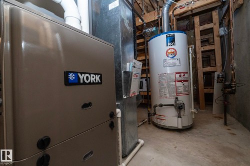 Utility area featuring a water heater, furnace, concrete flooring, and exposed structural elements - 25 1904 Mill Woods Road Road, Edmonton, AB - Indoor Photo Showing Basement