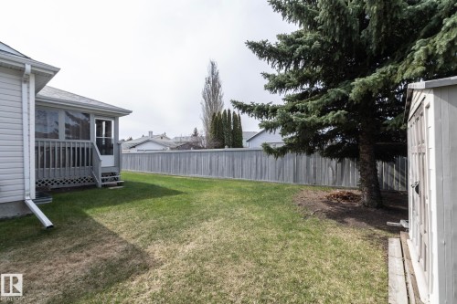 Expansive backyard featuring a screened-in porch with wood railing, a mature evergreen tree, a wooden storage shed, and a privacy fence - 25 1904 Mill Woods Road Road, Edmonton, AB - Outdoor With Deck Patio Veranda