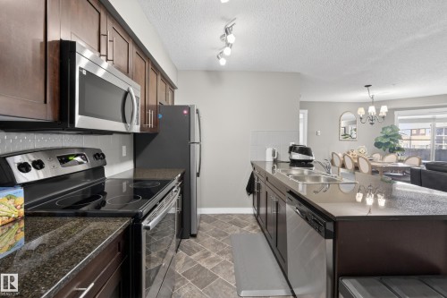 Contemporary kitchen featuring dark wood cabinetry, granite countertops, and stainless steel appliances - 314 3211 James Mowatt Trail Sw, Edmonton, AB - Indoor Photo Showing Kitchen With Stainless Steel Kitchen With Double Sink