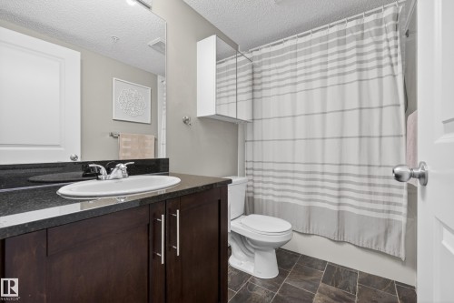 Bathroom featuring dark wood-finish vanity with an undermount sink, dark countertop, and large wall-mounted mirror - 314 3211 James Mowatt Trail Sw, Edmonton, AB - Indoor Photo Showing Bathroom