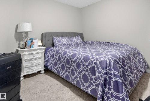 Carpeted room featuring light gray walls, a textured ceiling, and a built-in upholstered headboard - 314 3211 James Mowatt Trail Sw, Edmonton, AB - Indoor Photo Showing Bedroom