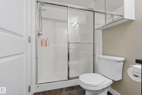 Three-piece bathroom featuring a shower with sliding glass doors, a built-in shower shelf, and a wall-mounted medicine cabinet with integrated lighting - 314 3211 James Mowatt Trail Sw, Edmonton, AB - Indoor Photo Showing Bathroom