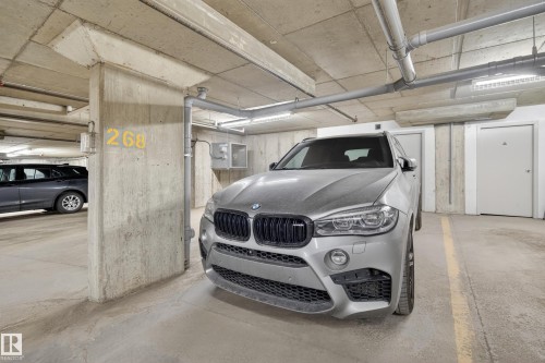 Dedicated parking stall within a concrete garage structure, featuring overhead lighting and visible utility piping - 314 3211 James Mowatt Trail Sw, Edmonton, AB - Indoor Photo Showing Garage