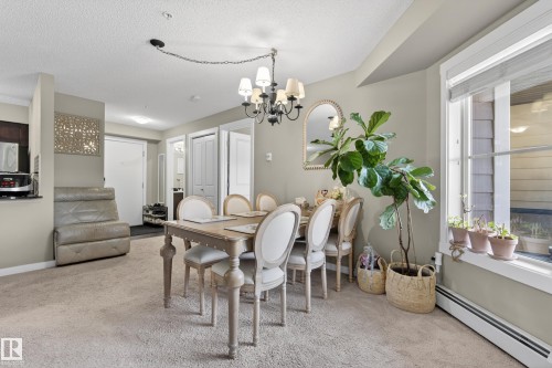 Open-concept dining area featuring a chandelier, a large window, and light-colored carpeting - 314 3211 James Mowatt Trail Sw, Edmonton, AB - Indoor Photo Showing Dining Room