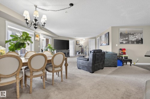 Spacious living area featuring light-toned carpeting, ample natural light from large windows, and a classic chandelier - 314 3211 James Mowatt Trail Sw, Edmonton, AB - Indoor