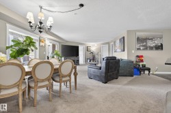 Spacious living area featuring light-toned carpeting, ample natural light from large windows, and a classic chandelier - 