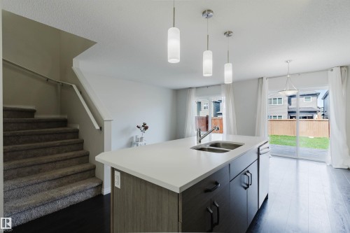 Kitchen island with an undermount double-basin sink, white countertop, and dark cabinetry - 2082 Price Landing, Edmonton, AB - Indoor Photo Showing Kitchen With Double Sink