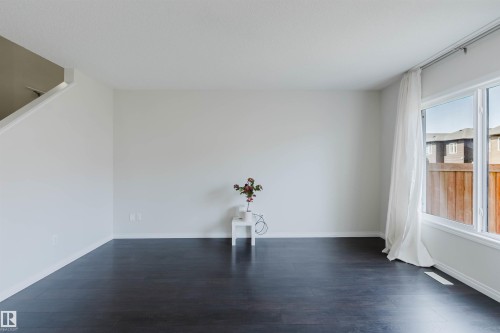 Spacious interior featuring dark wood-finish flooring, light neutral wall paint, and a large window with white trim - 2082 Price Landing, Edmonton, AB - Indoor Photo Showing Other Room