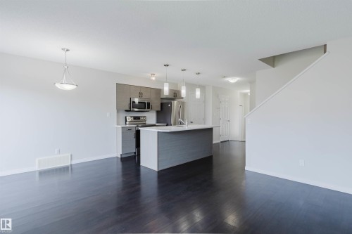 Open-concept living area featuring dark wood-finish flooring, a modern kitchen island with white countertop, stainless steel appliances, contemporary cabinetry, and a clean white color palette - 2082 Price Landing, Edmonton, AB - Indoor Photo Showing Kitchen