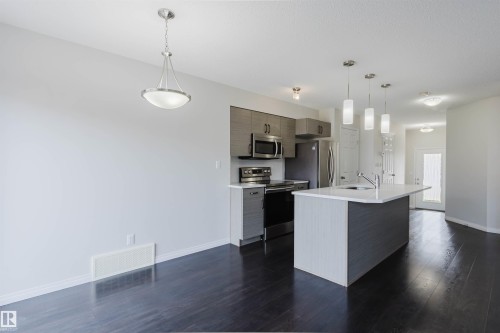 Open-concept kitchen featuring dark wood-finish flooring, stainless steel appliances, a center island with pendant lighting, and contemporary cabinetry - 2082 Price Landing, Edmonton, AB - Indoor Photo Showing Kitchen With Upgraded Kitchen