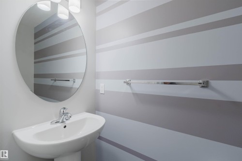 Contemporary bathroom featuring a pedestal sink with chrome faucet, an oval frameless mirror, and a three-light vanity fixture - 2082 Price Landing, Edmonton, AB - Indoor Photo Showing Bathroom