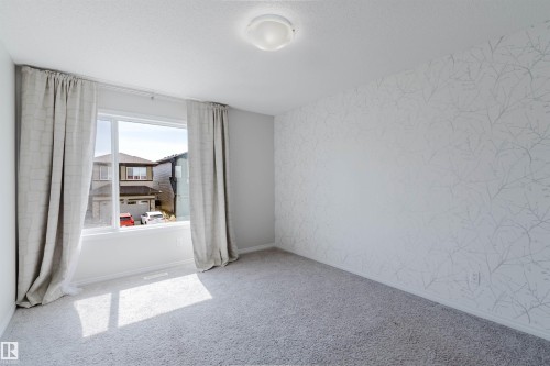 Spacious interior featuring a large window with drapes, patterned accent wall, light gray carpeting, and a ceiling-mounted light fixture - 2082 Price Landing, Edmonton, AB - Indoor Photo Showing Other Room