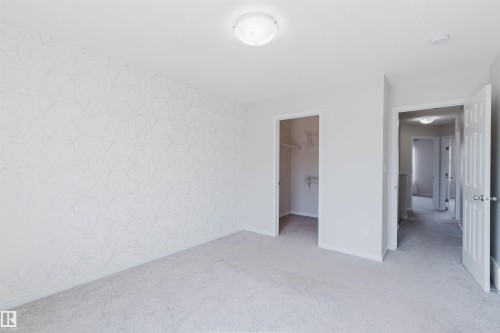 Carpeted room featuring a patterned accent wall, a flush-mount ceiling light, and a walk-in closet with shelving - 2082 Price Landing, Edmonton, AB - Indoor Photo Showing Other Room