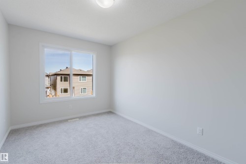 Bright interior room featuring a large window, soft gray carpeting, white baseboards, a white ceiling, and a flush-mount ceiling light fixture - 2082 Price Landing, Edmonton, AB - Indoor Photo Showing Other Room
