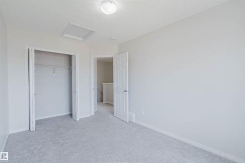 Carpeted room with bright white walls, featuring a bi-fold door closet with wire shelving, a white paneled door, and a flush mount ceiling light - 2082 Price Landing, Edmonton, AB - Indoor Photo Showing Other Room