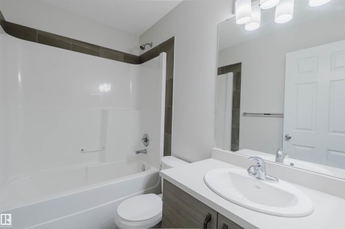 Bathroom featuring a shower/tub combination with a two-tone tiled surround, a toilet, a vanity with a white countertop and integrated sink, and an overhead vanity light fixture - 2082 Price Landing, Edmonton, AB - Indoor Photo Showing Bathroom